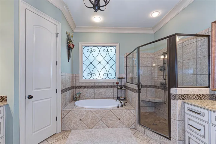 An elegant bath space features detailed tile surrounds, a built-in tub, and a separate glass shower.