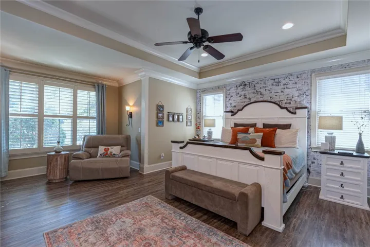 Elegant crown molding and a deep tray ceiling frame this spacious hardwood-floored bedroom.