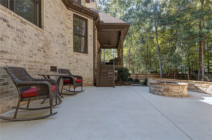 An expansive concrete patio features a built-in stone fire pit set against a brick exterior.
