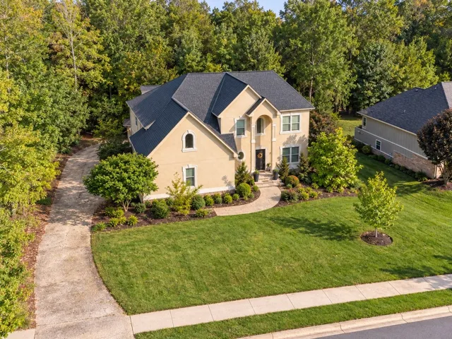 Mature trees frame a classic stucco facade and manicured lawn.