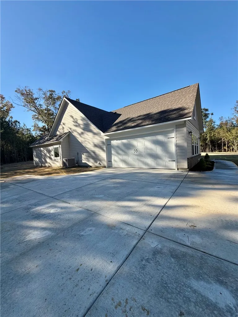 An expansive concrete driveway leads directly to a modern side-load garage structure.