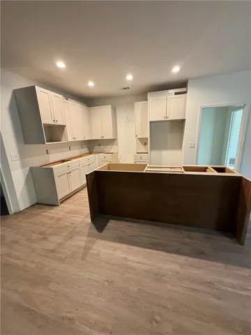 A spacious kitchen in progress features recessed lighting and smooth wood-textured flooring.