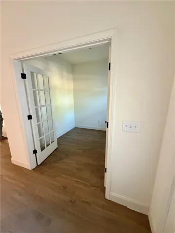 Double French doors open into a versatile home office featuring warm wood flooring.