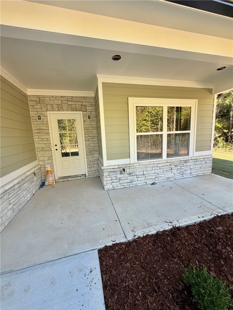 An inviting covered concrete entryway welcomes guests with clean stone veneer accents and lap siding.