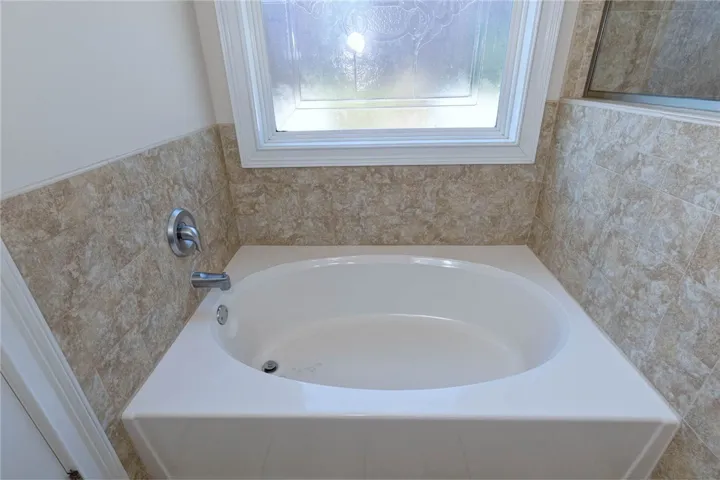 A deep soaking tub sits enveloped in classic textured tile wainscoting beneath a large window.