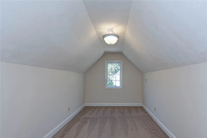 Angled ceilings frame a cozy bonus space featuring soft wall-to-wall carpeting and a central window.
