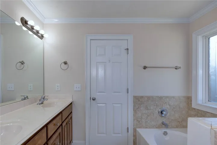 A spacious bathroom features a double vanity and a built-in soaking tub alongside classic molding.