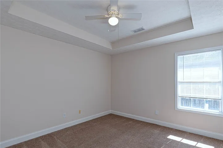 An elegant tray ceiling and soft carpeting define this inviting and versatile bedroom space.