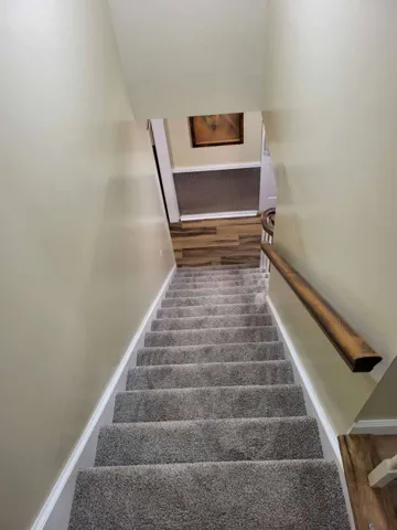 A carpeted staircase features a classic wooden handrail leading down to a wood-look floor.