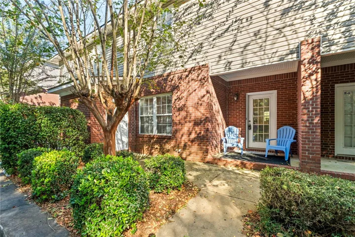 Mature plantings flank a welcoming brick-paved entry walkway leading to a glass-paneled front door.