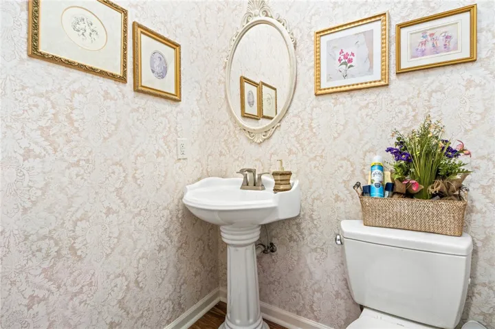An elegant powder room features a classic pedestal sink and detailed patterned wallpaper.