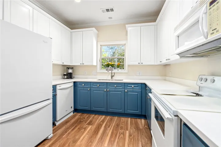 Rich wood-patterned flooring pairs with classic two-tone cabinetry underneath a centered garden-view window.