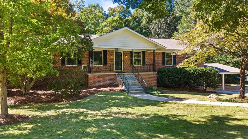 Mature trees frame a classic brick ranch home featuring an elevated front porch.