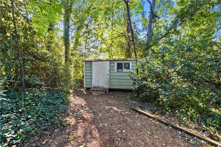 A practical storage shed stands nestled within a shaded, wooded area of the property.