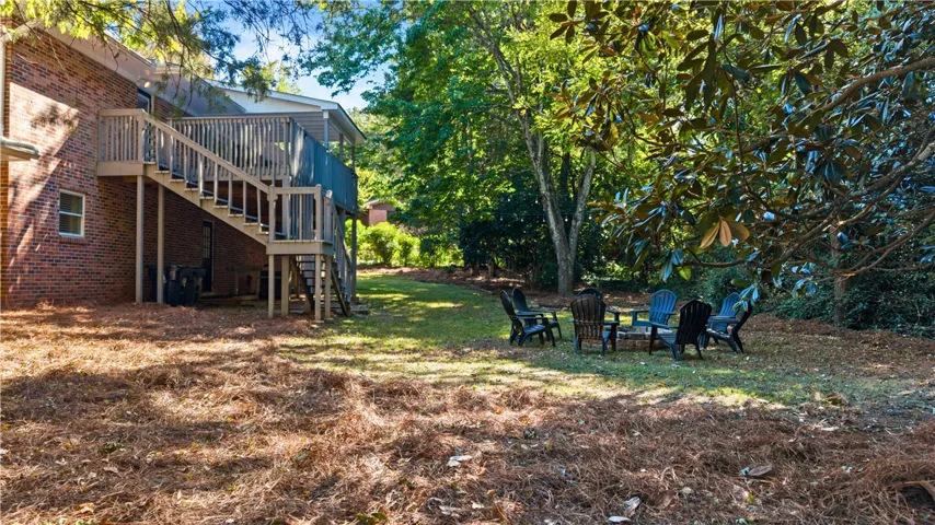 Mature trees frame a grassy yard featuring a multi-level wooden deck and dedicated fire pit area.