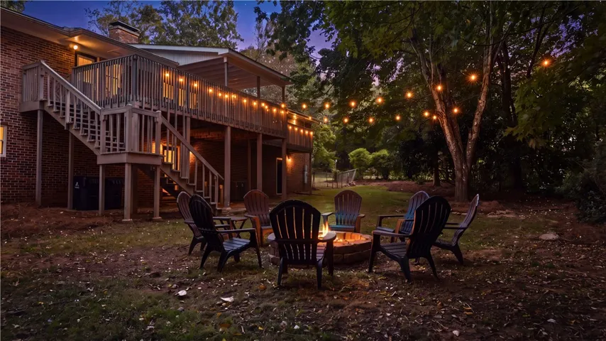 An expansive multi-level wooden deck overlooks a grassy backyard complete with a stone fire pit.