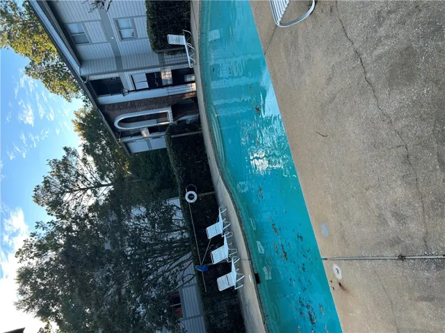 A community swimming pool is bordered by concrete decking and lush green hedges.