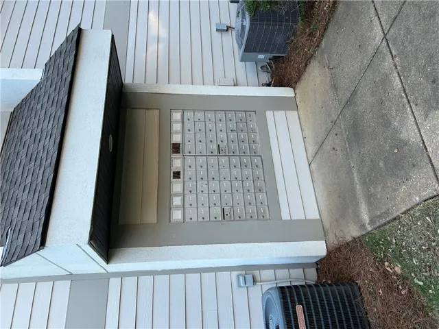 Shingled overhang shields a central bank of outdoor mailboxes alongside a concrete walkway.