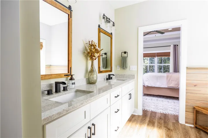 Double vanities with stone countertops align with modern wood-style flooring in this refined bathroom.