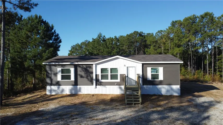 Mature trees frame a modern manufactured home featuring clean vertical siding and simple entry steps.