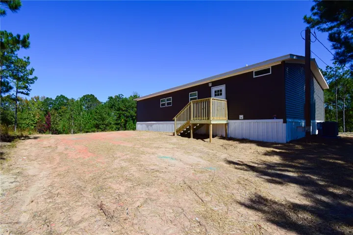 A spacious clearing surrounds the modern structure, nestled against a backdrop of mature pine trees.
