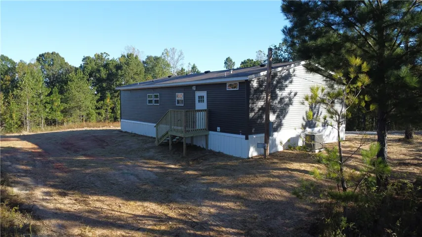 A spacious clearing surrounds this modern manufactured home featuring a simple wooden deck.