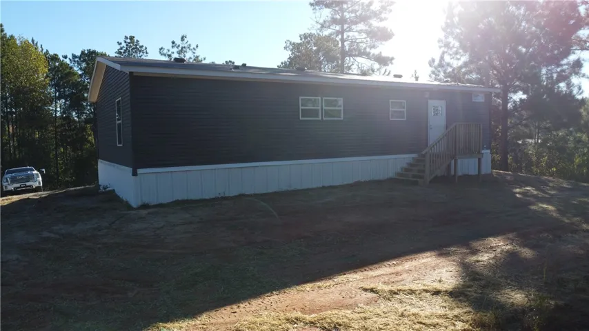 Mature trees frame a modern manufactured home featuring clean siding and a wooden entry staircase.