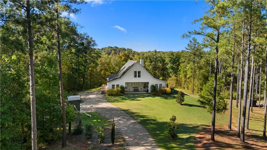 A secluded forest clearing surrounds this classic farmhouse retreat with an expansive green lawn.