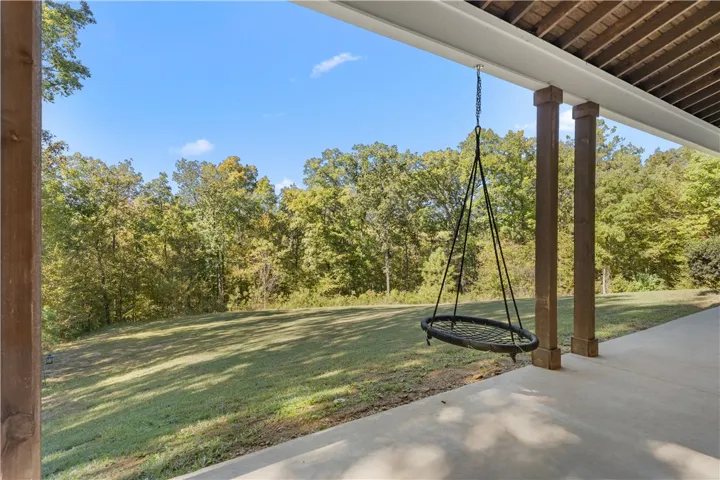 A covered patio overlooks a lush lawn framed by mature trees.