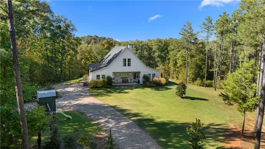 A long gravel driveway leads toward this modern farmhouse nestled in a private forest setting.