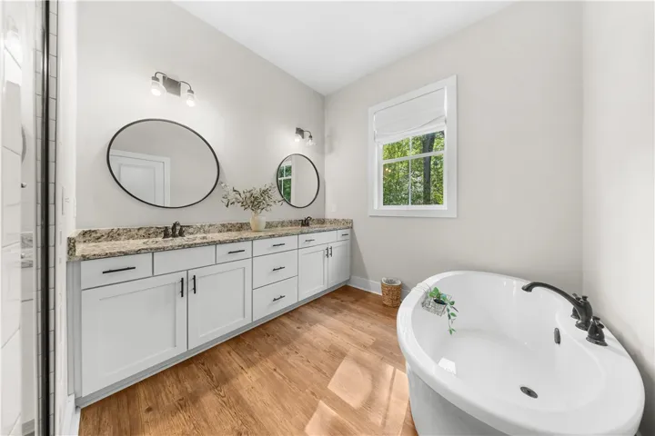 Warm wood flooring contrasts with a stone-topped double vanity and a deep soaking tub.