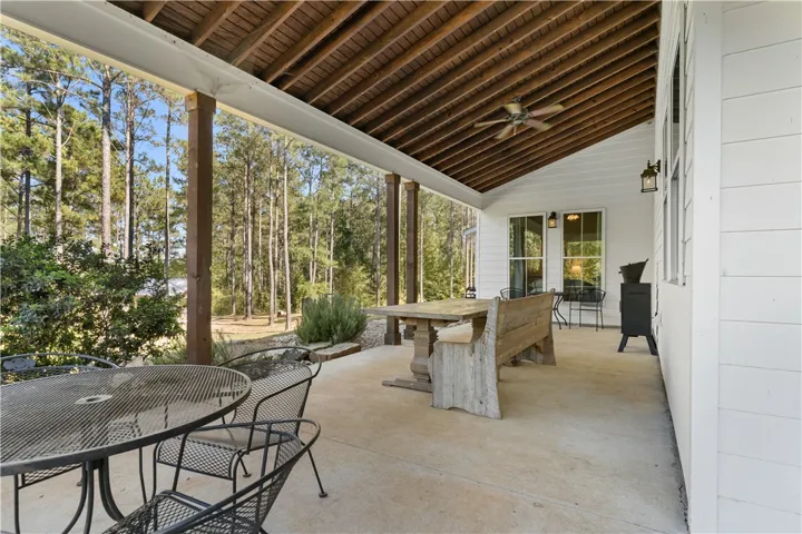 An expansive covered patio features exposed wood ceiling joists and peaceful views of the surrounding woods.