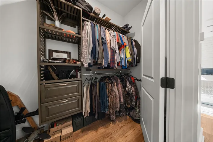 An organized walk-in closet boasts custom built-in shelving, hanging rods, and rich hardwood flooring.