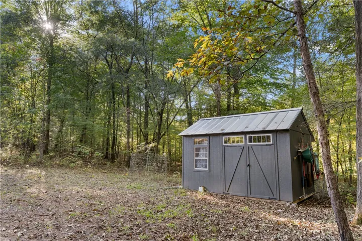 A detached storage building stands nestled among mature trees on the wooded property.