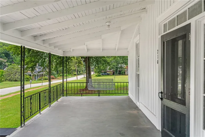 A spacious covered porch features concrete flooring, classic beadboard siding, and a decorative metal railing.