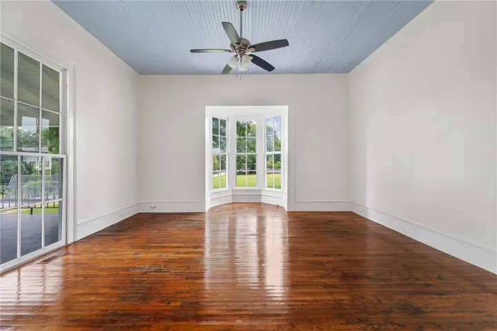 Rich hardwood flooring anchors this versatile space featuring a charming bay window.