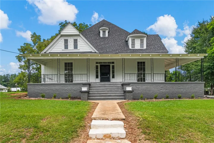An inviting front porch overlooks the spacious lawn under a clear blue sky.