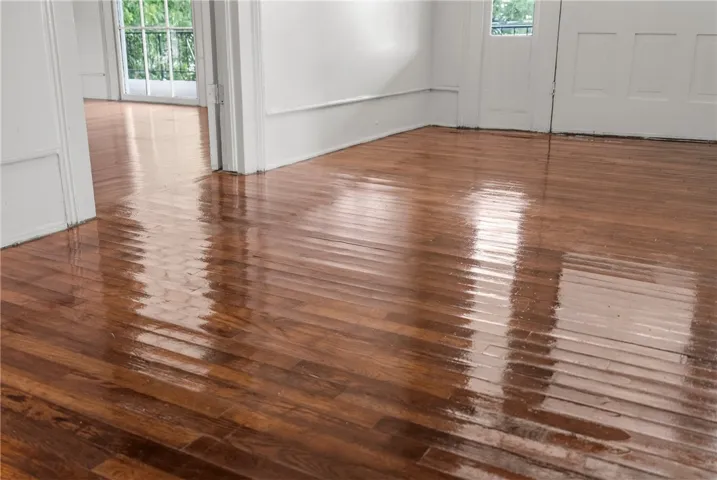 Polished hardwood floors reflect the natural light pouring through classic glass doors.