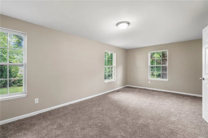 Multiple windows draw natural light into this bedroom finished with wall-to-wall carpeting.