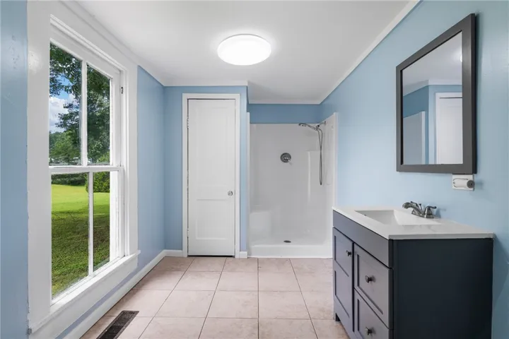 A light-filled bathroom displays clean tiled flooring, a modern vanity, and a glass-free walk-in shower.