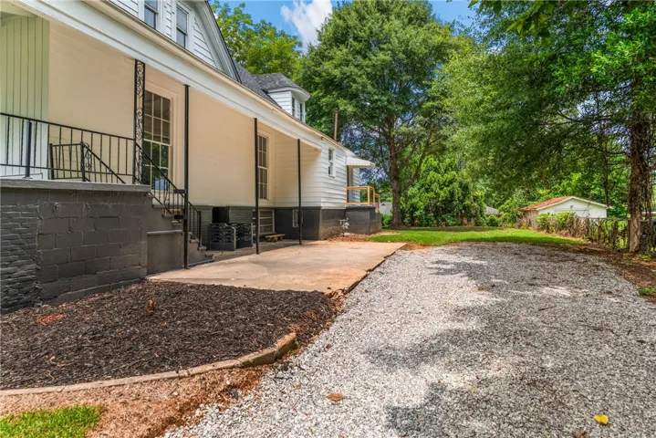 A spacious gravel driveway and concrete patio frame the side entry of this classic home.
