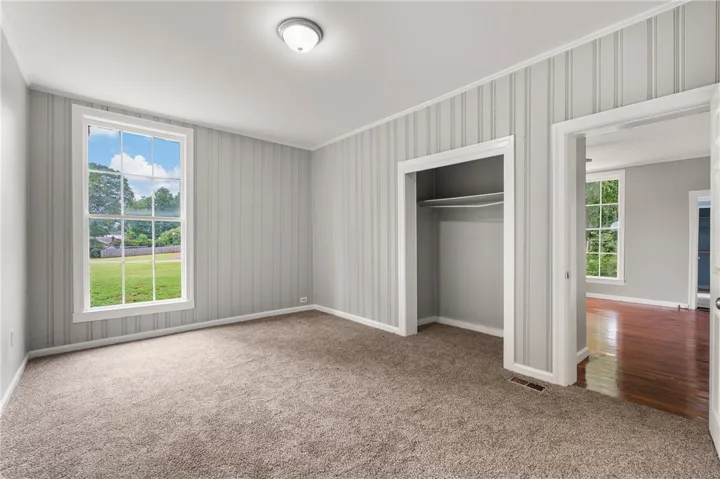 A spacious bedroom features neutral carpeting, a classical window, and an open closet recess.