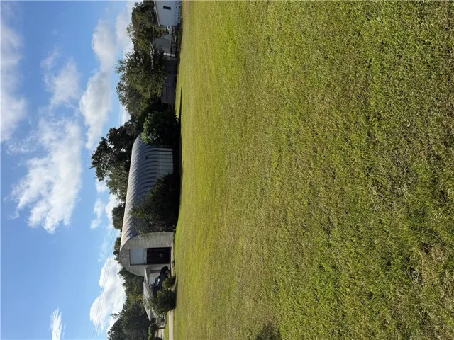 A spacious grassy lawn borders functional outbuildings under a clear blue sky.