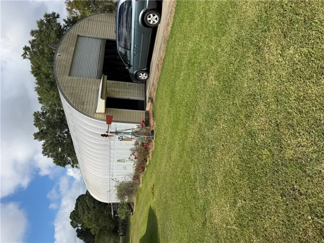 A spacious metal workshop is bordered by expansive green lawn under a partly cloudy sky.