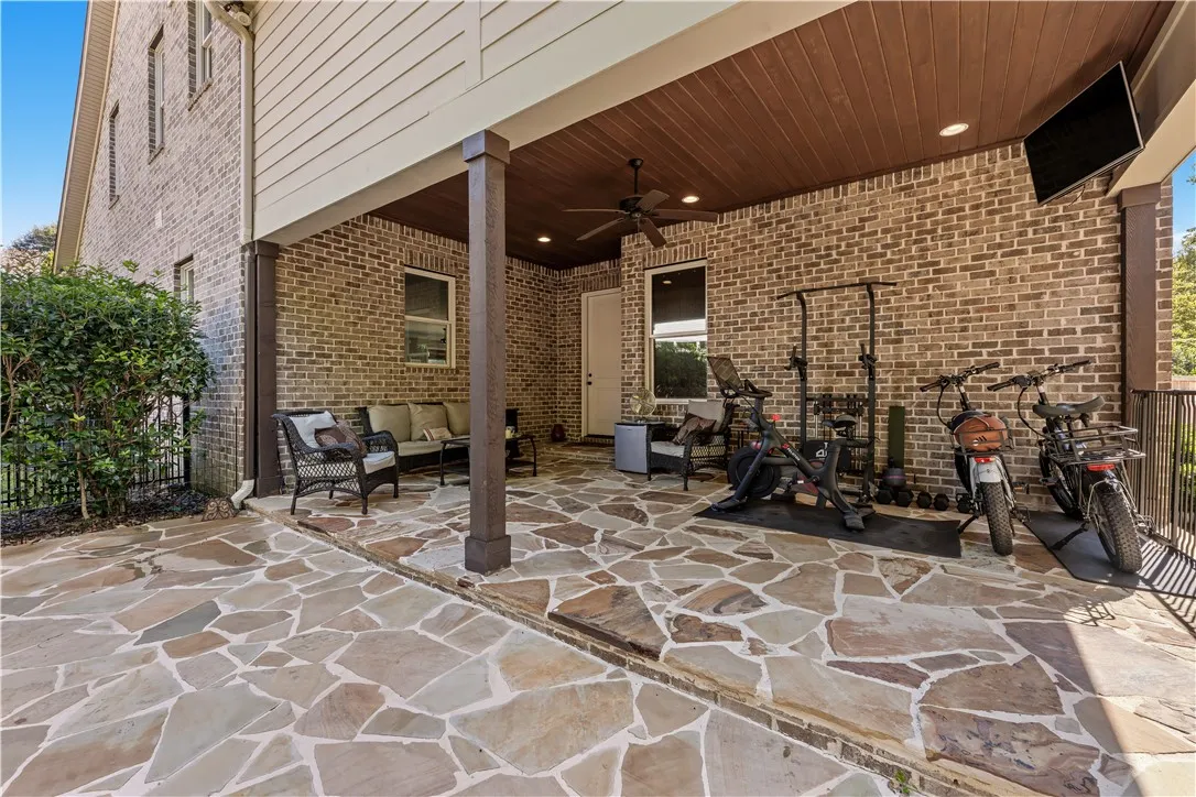 A spacious stone patio sits beneath a covered wood-paneled ceiling alongside brick exterior walls.