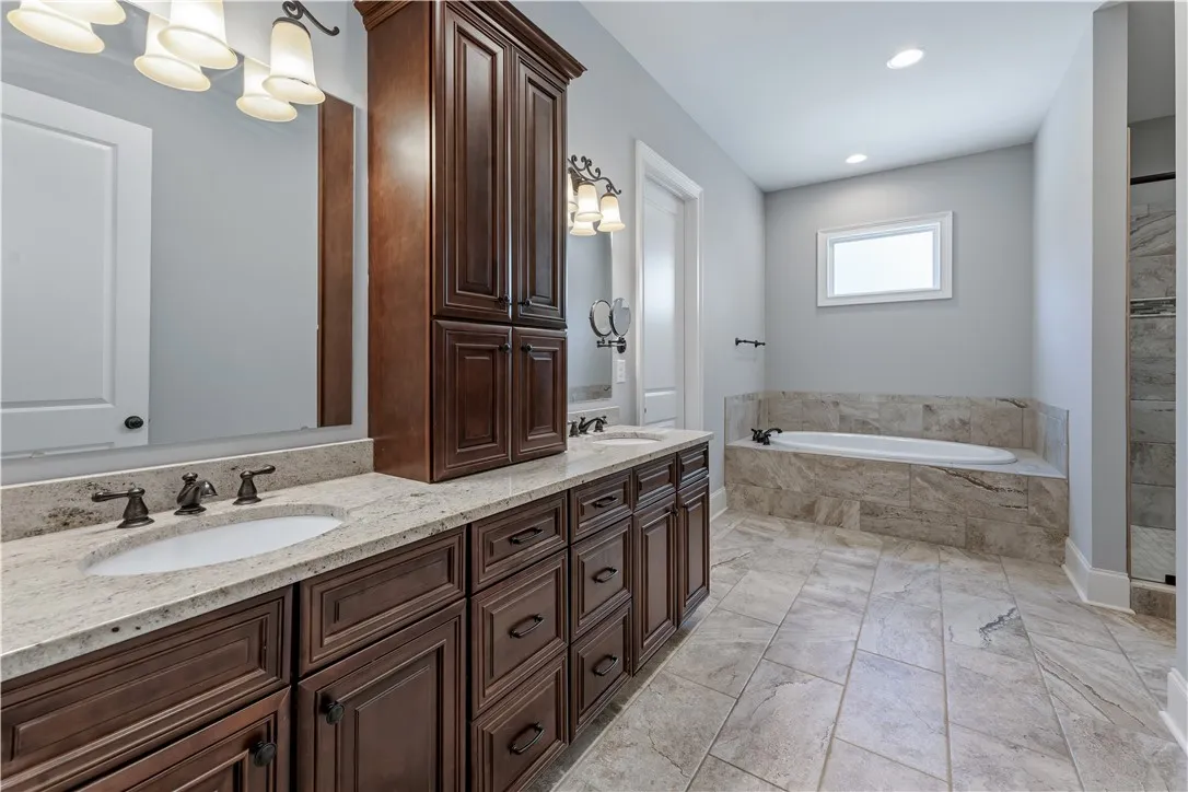 Rich wood cabinetry contrasts with neutral stone tiling in this well-appointed bathroom.