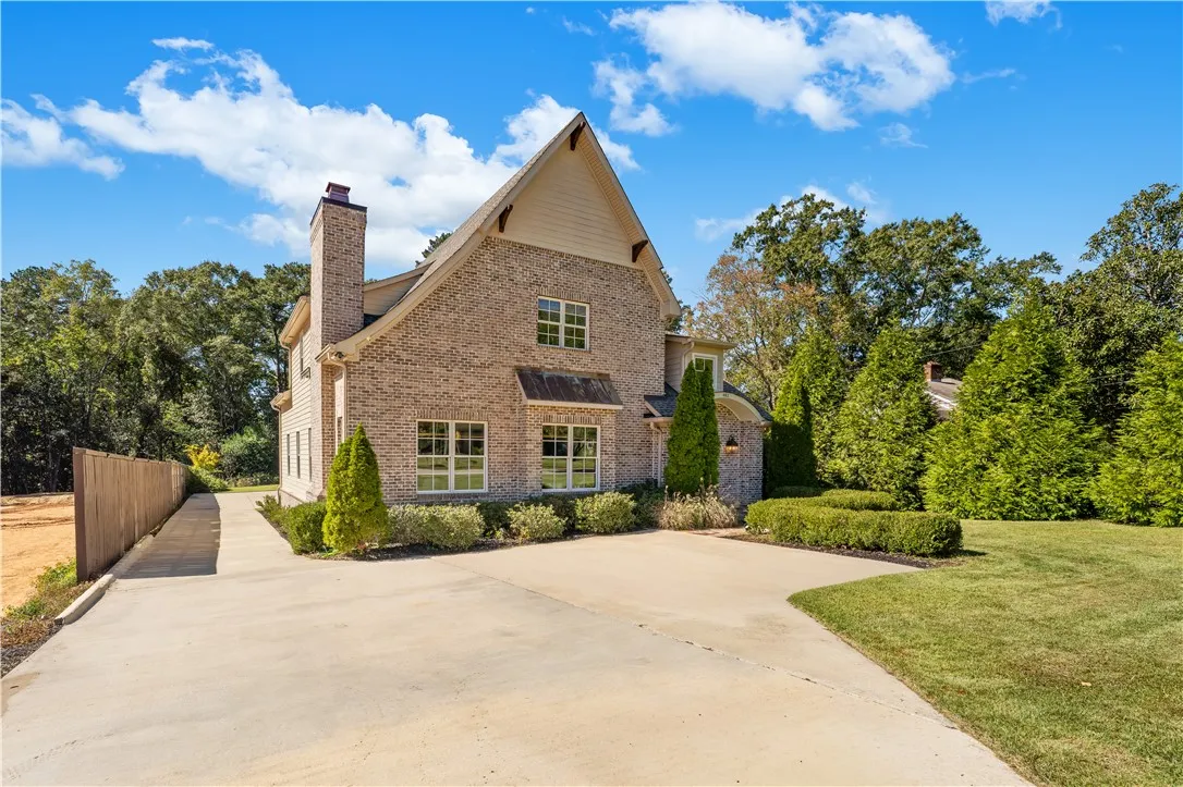 An impressive multi-story brick exterior rises from a spacious concrete driveway framed by manicured lawns.