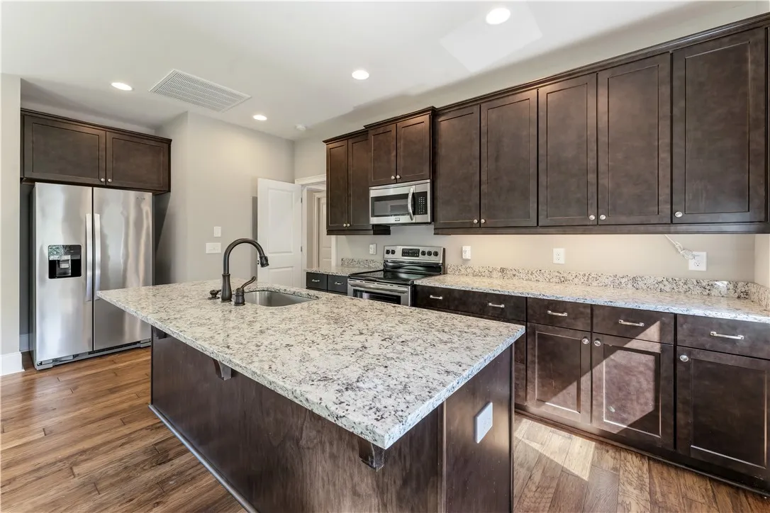 Rich dark wood cabinetry pairs with light granite countertops and hardwood flooring in this kitchen.