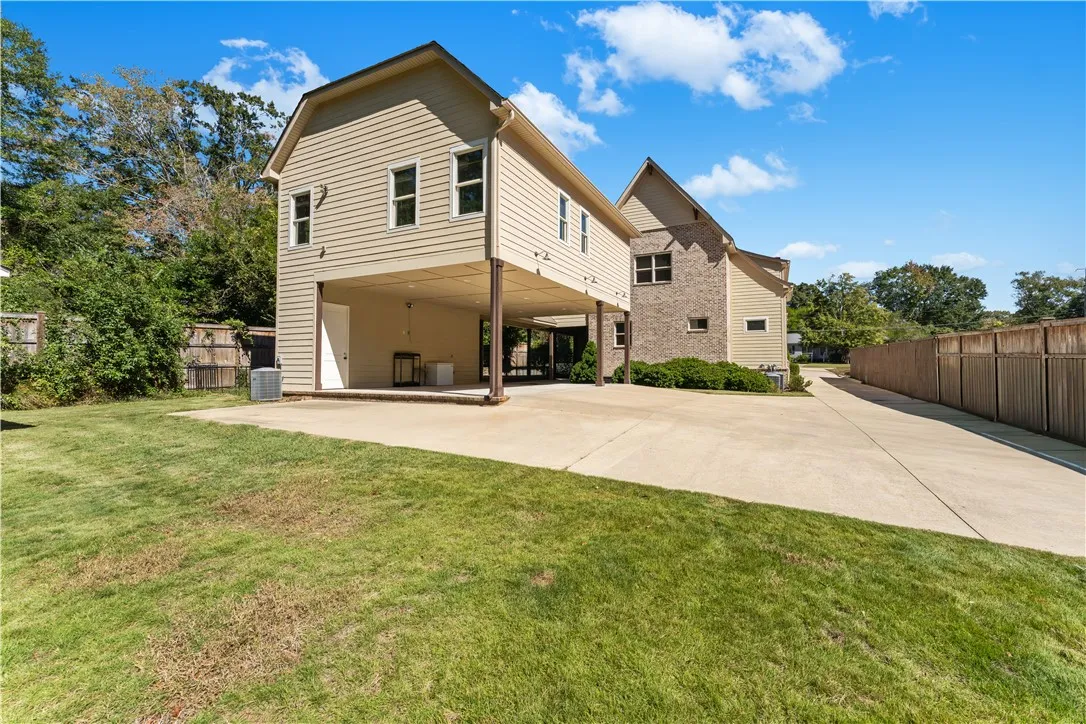An expansive concrete driveway leads to a covered carport alongside a manicured lawn.