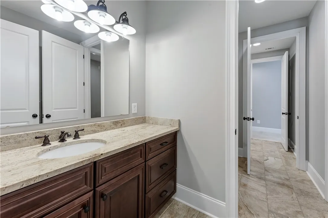 Granite counters and rich wood cabinetry anchor this elegant secondary bath with clean tile flooring.